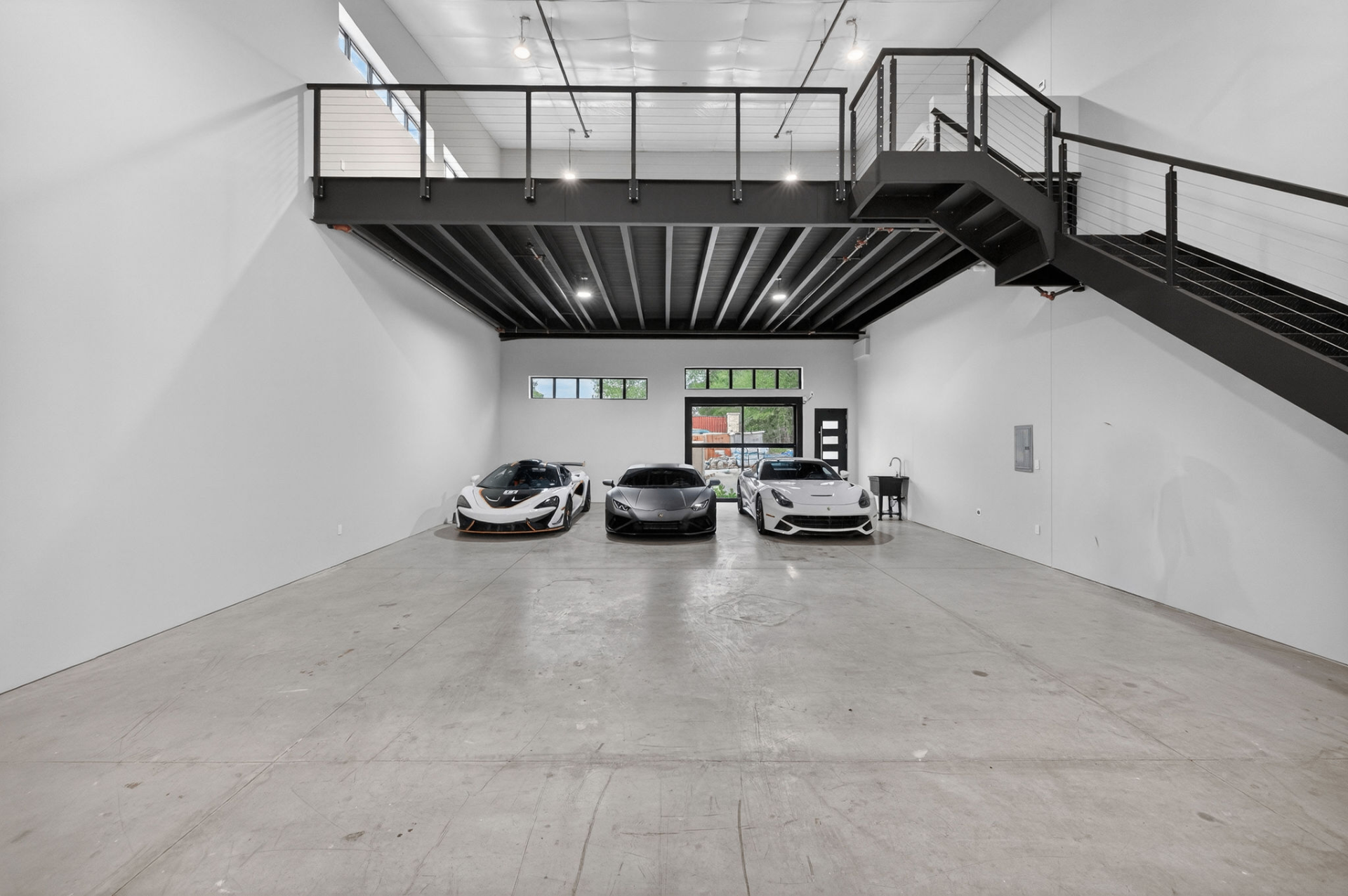 Three supercars parked inside a GOTA Autominium with steel mezzanine and staircase above