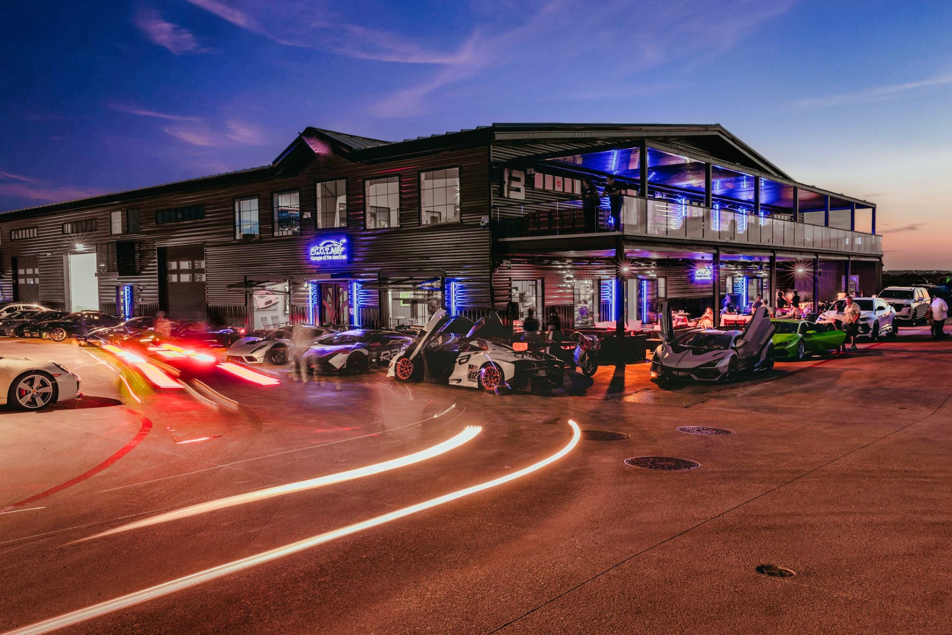 GOTA clubhouse at dusk with supercars and light trails out front