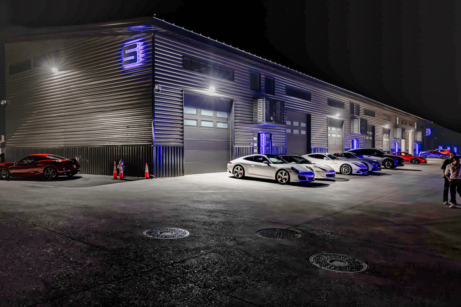 GOTA Autominium exterior at night with blue accent lighting and supercars parked outside