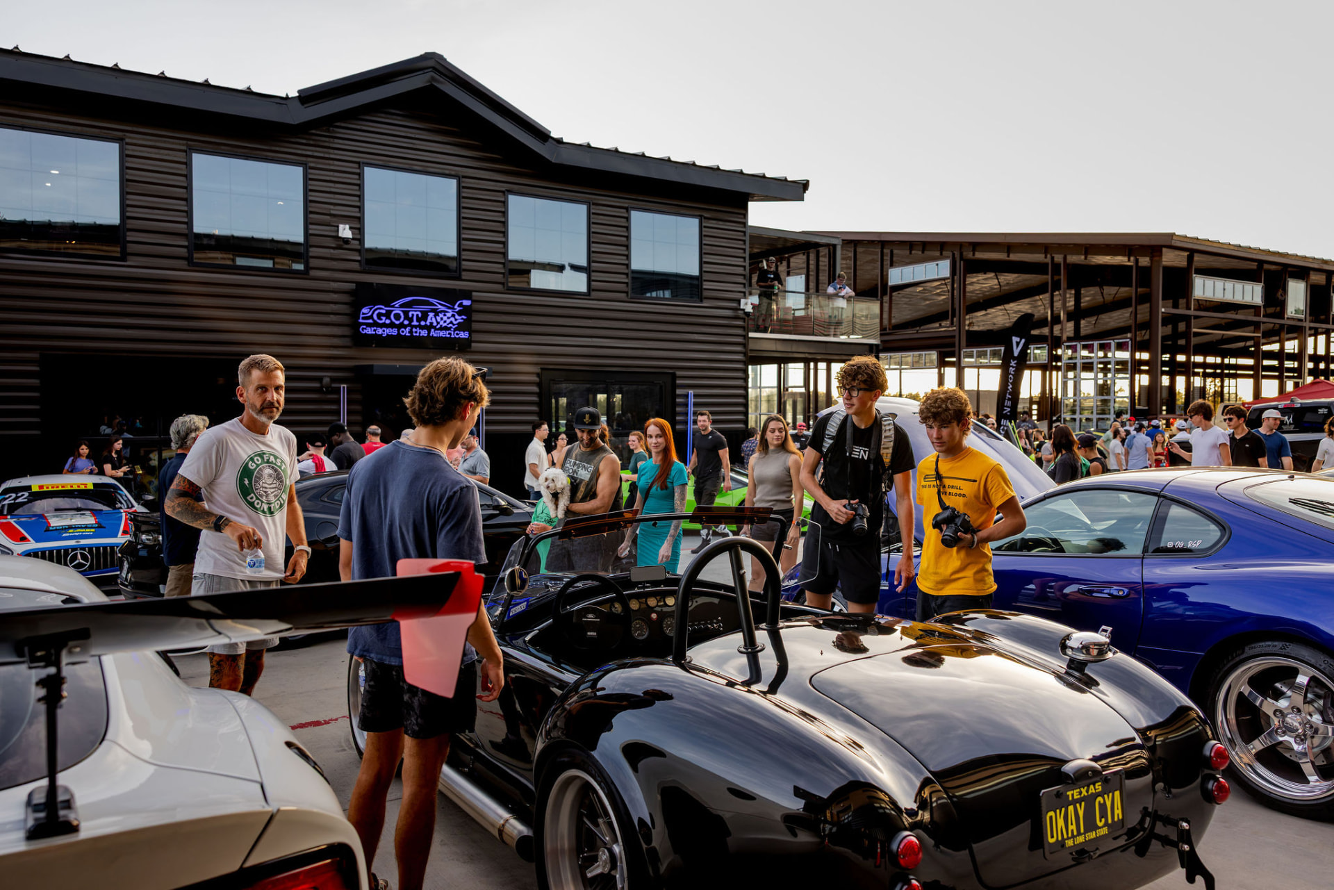 Owners and photographers around a Shelby Cobra outside the GOTA clubhouse